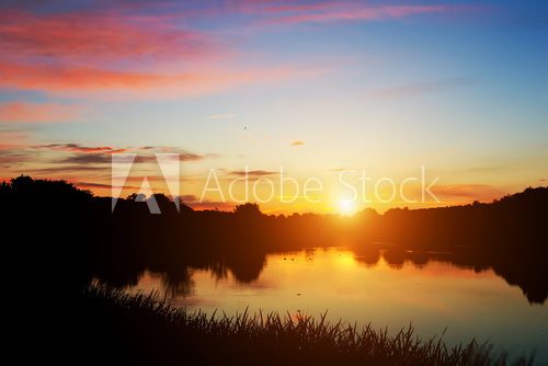 Lake in forest at sunset. Romantic sky with red clouds