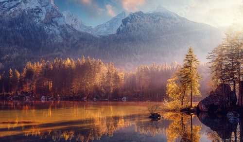 Awesome Nature Scenery. Beautiful landscape with high mountains with illuminated peaks, stones in mountain lake, reflection, blue sky and yellow sunlight in sunrise. Amazing nature Background.