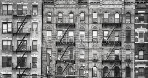 Black and white picture of old buildings with fire escapes, one of the New York City symbols, USA.