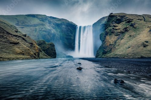 Dark night view of Skogafoss Waterfall. Fantastic summer landscape of Skoga river. Amazing outdoor scene of Iceland, Europe. Beauty of nature concept background.