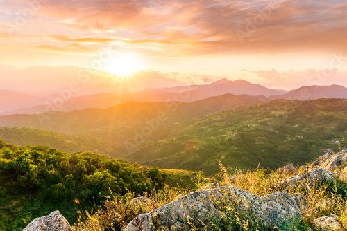 highland mountain landscape of beautiful sunset or sunrise with nice mountain peaks and slopes, green and golden hills and majestic cloudy sky on background