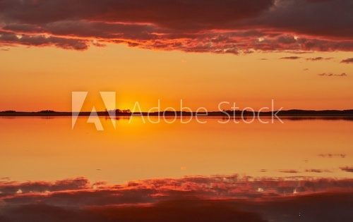 Orange and red sky after the sunset at a lake in Finland. Symmetrical reflection of clouds in the still water.