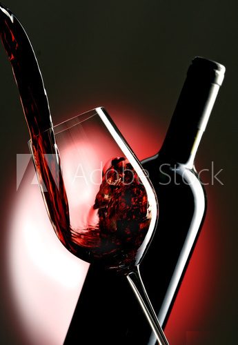 Pouring red vine into glass with bottle in the background