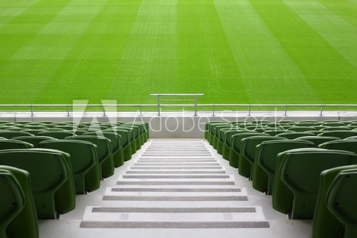 Rows of folded, green, plastic seats in very big, empty stadium 