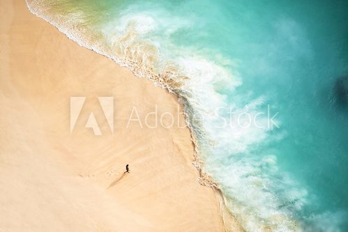 View from above, stunning aerial view of a person walking on a beautiful beach bathed by a turquoise sea during sunset. Kelingking beach, Nusa Penida, Indonesia.